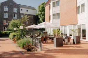 a patio with tables and umbrellas in front of a building at Parkhotel Papenburg by Hackmann in Papenburg