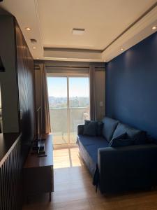 a living room with a blue couch and a large window at Flat Red Sorocaba - Blue in Sorocaba