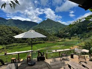 a deck with an umbrella and chairs and mountains at Bản Sù - Homestay in Sapa