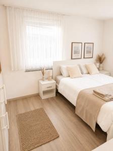 a white bedroom with two beds and a window at STAY - Comfort Apartment in Friedrichshafen
