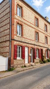 a brick building with red shutters on a street at Le bleu infini - vue mer, falaises, centre ville in Étretat