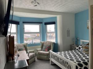 a bedroom with blue walls and a bed and chairs at Henry's On The Prom in Great Yarmouth