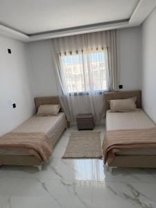 two beds in a white room with a window at Lux appartement S plus deux a hay el wahat in El Aouina Station