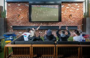 a group of people sitting on a couch watching a soccer game at Tonsley Hotel in Adelaide