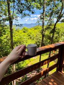 a person holding a cup of coffee on a fence at Cabanas do Bosque in Três Coroas +1 photo