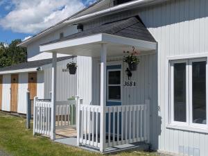 a white house with a porch with potted plants on it at Le Repere, Beach, Whales, and Ferry in Saint-Siméon