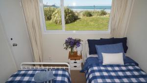a bedroom with two beds and a window with a view at Hideaway Beach Cottage in Curio Bay