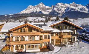 a house in the snow with mountains in the background at Appartements-Pension Renberg in Maria Alm am Steinernen Meer