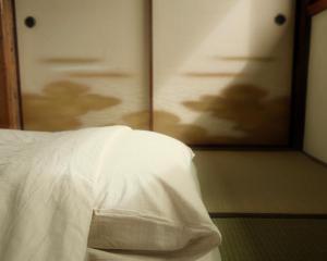 a bed with white sheets and a door with a painting at Omoya Kitahata in Karatsu