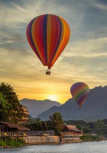 two hot air balloons flying over the water at sunset at Amari Vang Vieng in Vang Vieng