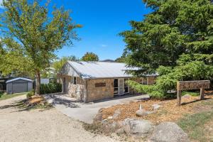 a stone house with a gravel driveway and trees at Rock On Cottage in Jindabyne