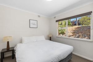a white bedroom with a bed and a window at Rock On Cottage in Jindabyne