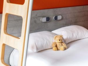 a teddy bear sitting on a bed with pillows at Ibis Budget Marmande in Marmande