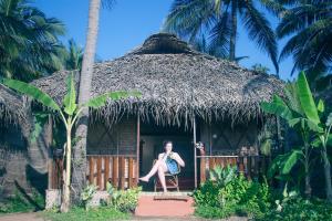 a woman sitting in a chair in front of a hut at Mariposa Beach Grove in Agonda