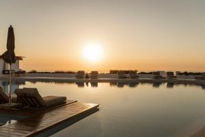 a pool with lounge chairs and the sun setting at NĒRO Boutique Hotel in Imerovigli