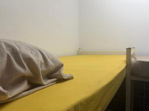 a bed with a yellow sheet and a pillow on it at Beach hostel in Muscat
