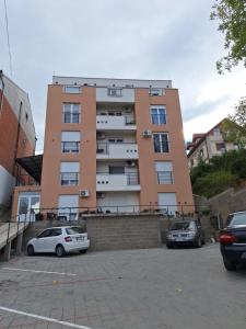 a tall building with cars parked in a parking lot at Apartman MILOVANOVIĆ in Vrnjačka Banja