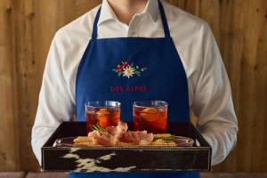 a person holding a tray of food with two drinks at Hotel Des Alpes in La Villa