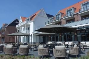 an outdoor patio with tables and chairs and umbrellas at Hotel The Dunes in Domburg