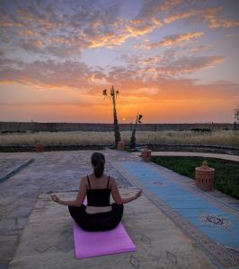 a woman sitting in a lotus position on a yoga mat at sunset at Dar Diyafa Marrakech in Maout