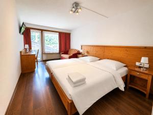 a bedroom with a large white bed and a chair at Hotel Alpenblick in Klosters