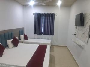 a room with two beds and a tv on the wall at HOTEL KRISHNAM Inn in Mathura