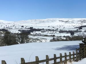 a snow covered hill with a fence and a field at Aysgill Cottage in Hawes