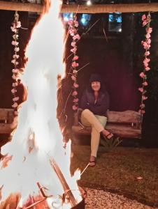 a woman sitting on a bench next to a fire at Pousada Canto do Sossego in Brumadinho