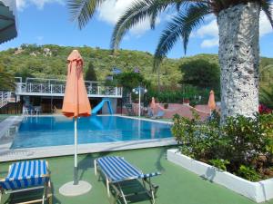 a swimming pool with two chairs and an umbrella at Villa Magdalena studios in Ágios Ioánnis