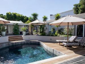 a pool with chairs and umbrellas next to a house at The Gregoire Boutique Villa in Hermanus