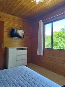 a bedroom with a bed and a tv and a window at Cabana Mais Natureza in Santo Amaro da Imperatriz
