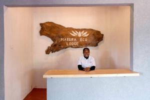 a man sitting at a counter with a sign on the wall at Marera Eco Lodge in Karatu