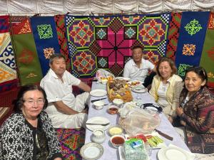 a group of people sitting around a table with food at Guest house Aibek in Kurmenty