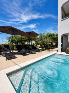 a swimming pool with chairs and umbrellas next to a building at Paulina Harmony Rooms in Seget Vranjica