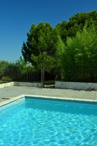 a blue swimming pool with a fence and trees at Les Mourguettes in Tulette