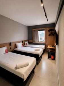a hotel room with three beds and a television at ibis Santos Gonzaga Praia in Santos