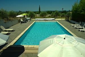 a swimming pool with an umbrella and some chairs at Les Mourguettes in Tulette