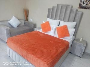 a bed with orange and white pillows and a couch at The Hush House in Roodepoort