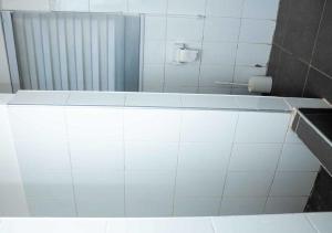 a white tiled bathroom with a tub and a mirror at Mycom Apartment in Kumasi