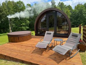 a wooden deck with two chairs and a fire pit at Kedras Glamping - Pod tipo nameliai in Prapuntai