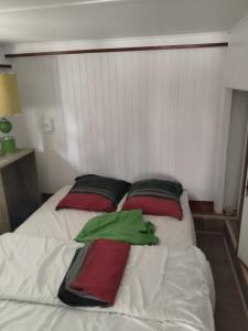 a white bed with red and green pillows on it at chalet les pieds dans l'eau in Neuvic