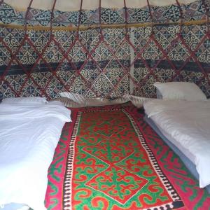 a room with two beds and a wall with a rug at Kapchygai Yurt Camp in Dzhetyoguz
