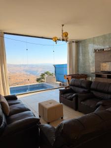 a living room with leather couches and a large window at Luxury Mountain Chalet with Private Pool Lionden Jerash in Jerash