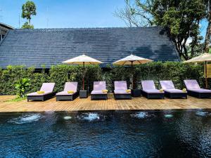 Eine Gruppe von Stühlen und Sonnenschirmen neben einem Pool in der Unterkunft MORA Boutique Hotel in Chiang Rai