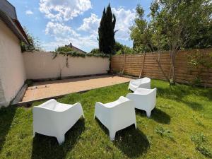 three white chairs sitting in the grass in a yard at Maison Cosy, proche Reims, La Nichée in Bazancourt