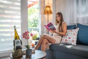 a woman sitting on a couch reading a book at Ezerjó Házikó in Nyúl
