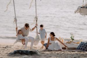 a family sitting on the beach with a swing at Khaolak Emerald Beach Resort and Spa in Khao Lak