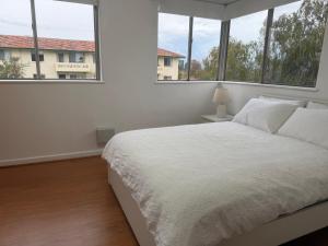 a bedroom with a white bed and windows at Como Beach Apartment 2 in Perth
