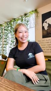 a woman sitting at a table smiles at the camera at The Evergreen Hostel 長期ステイ歓迎 エバーグリーンホステル in Hiroshima