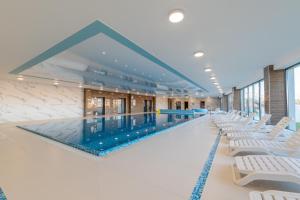 a large swimming pool with white chairs in a building at Navy Blue Apartment - SPA - Basen - Parking in Dziwnów